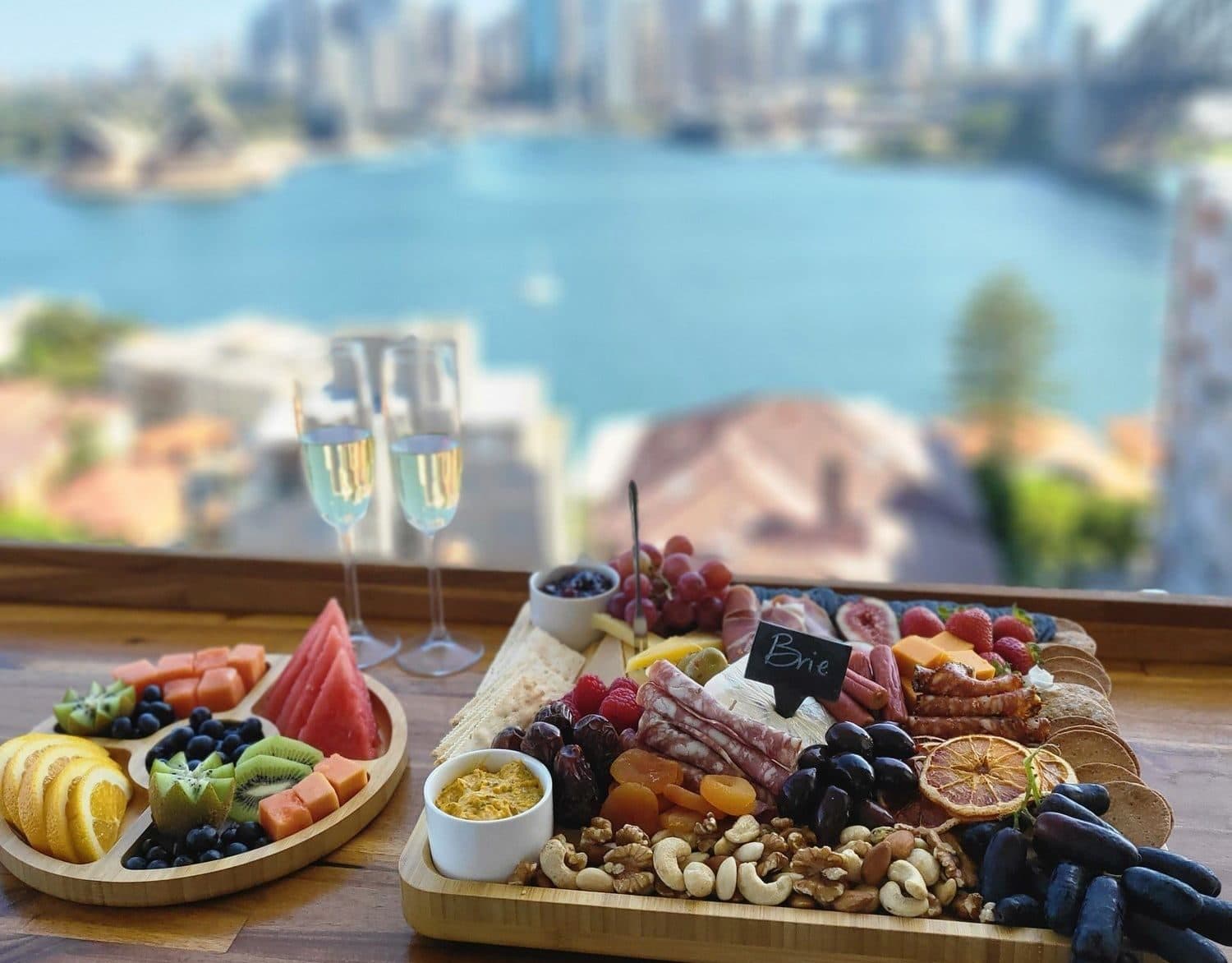 Table set with two loaded cheese boards and champagne, Sydney Harbour beyond