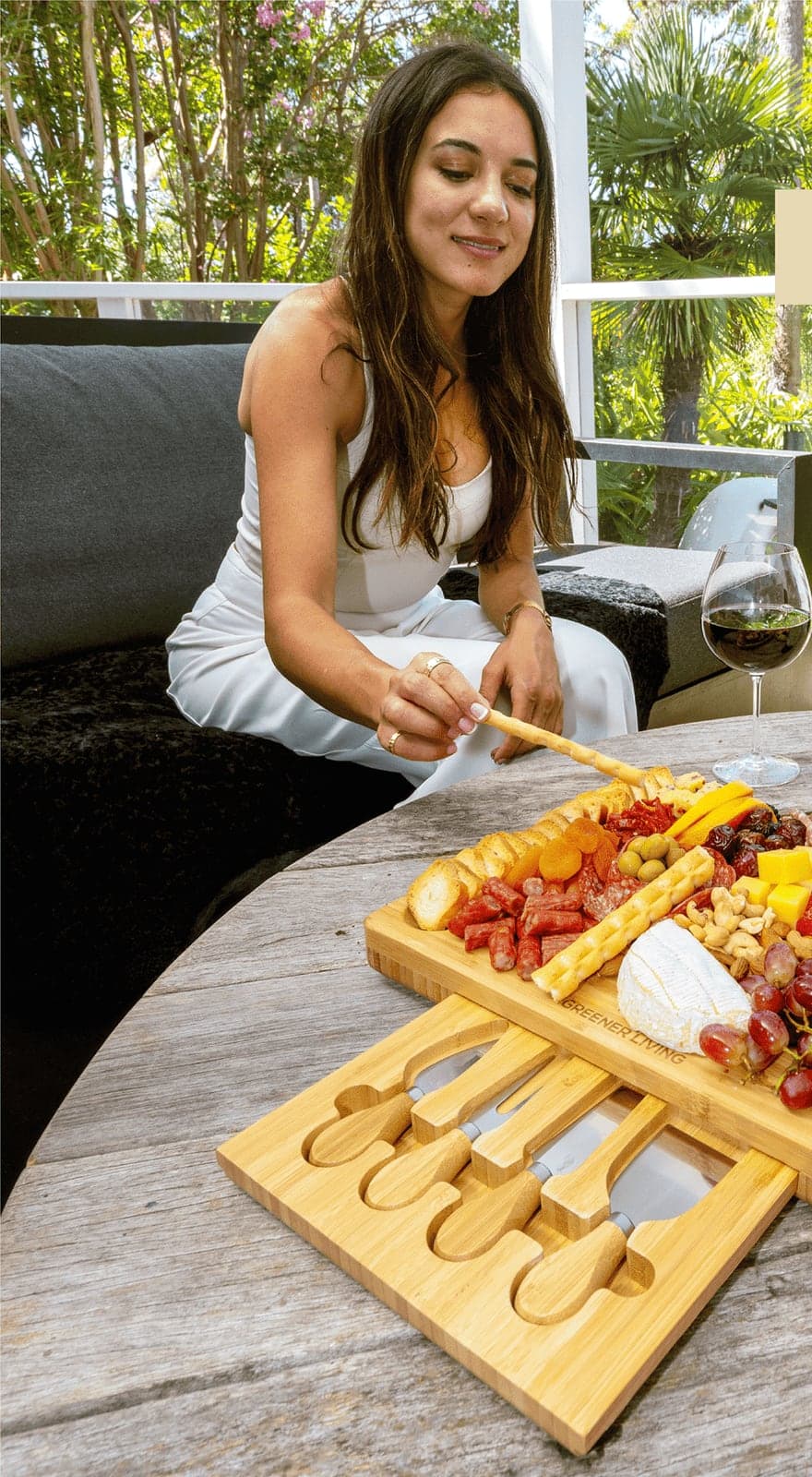 Woman picking food from the cheese board at an outdoor table with a glass of wine