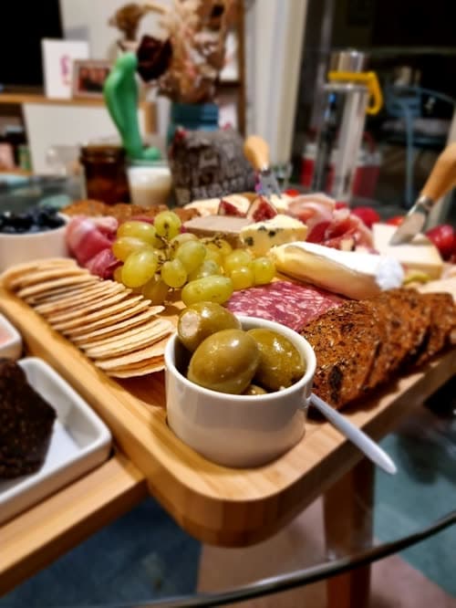Customer photo of the board loaded with grapes, crackers, olives and bread on a glass table