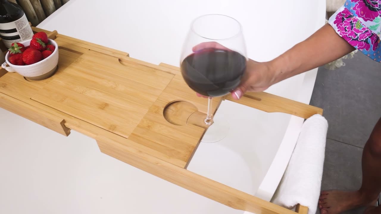 The bamboo caddy set across a bath holding a glass of red wine and a book