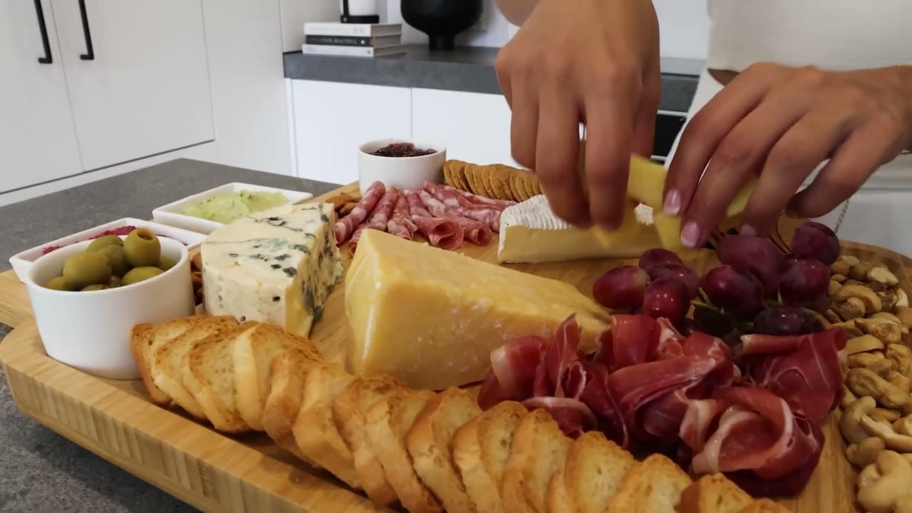 Hands arranging cheese, cured meats and crackers across the loaded board