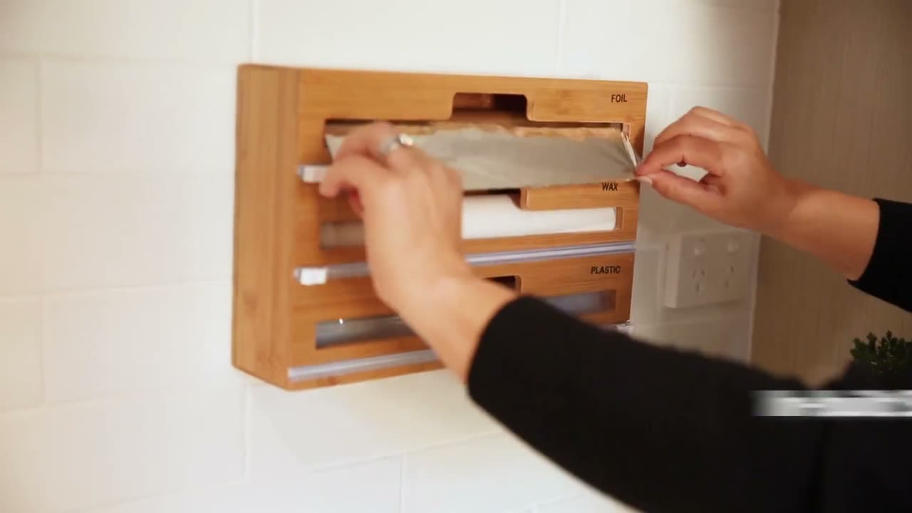 Hands pulling and cutting foil from the wall-mounted bamboo dispenser