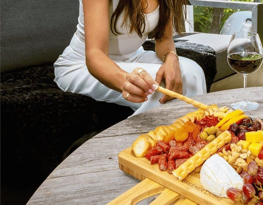 Hand reaching across a loaded cheese board and a glass of wine on an outdoor table