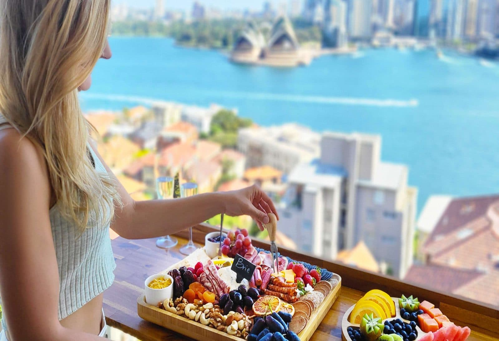 Woman plating a charcuterie board on a balcony above Sydney Harbour