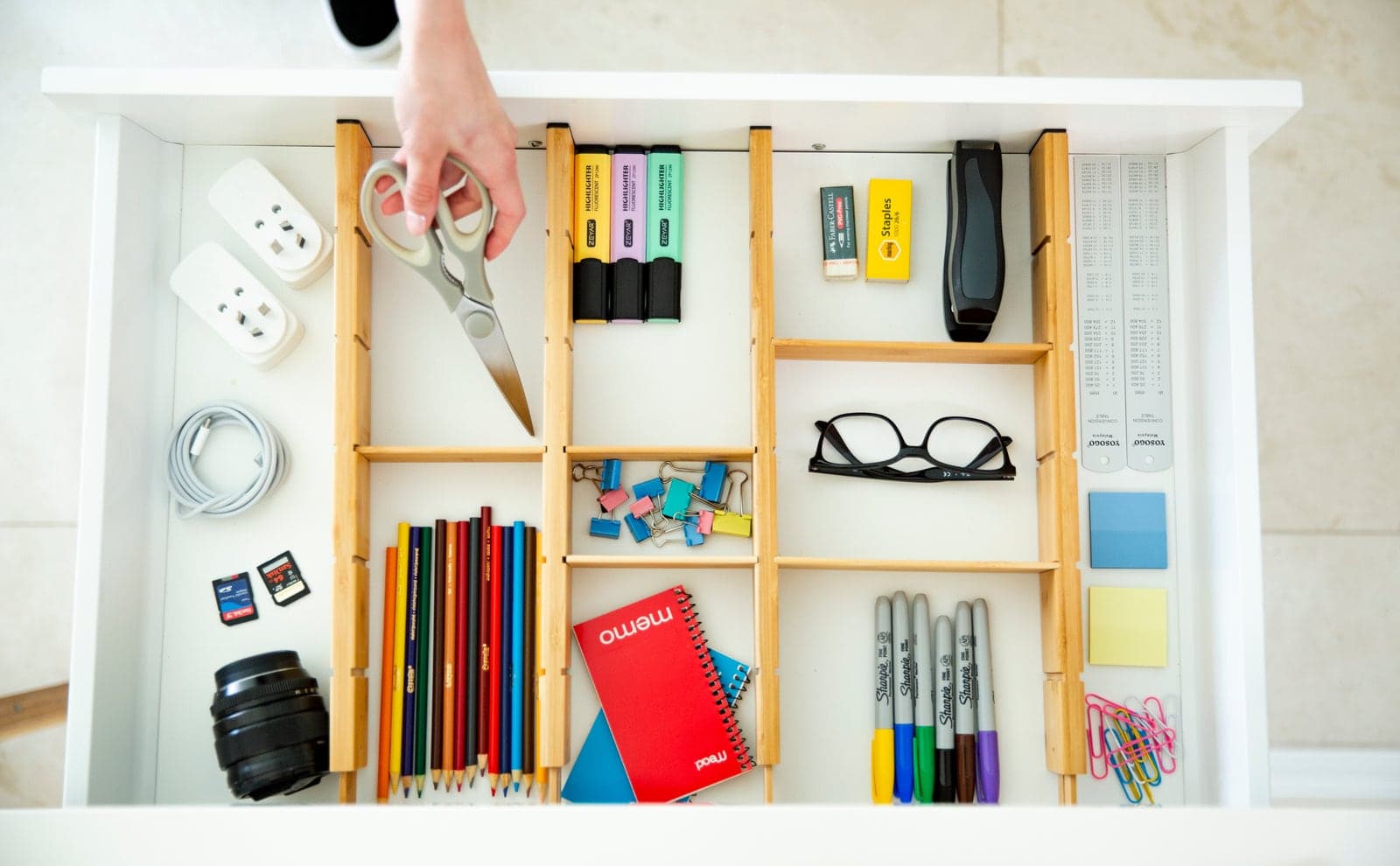 Overhead office drawer organised into bamboo divider compartments holding dice, scissors and pens